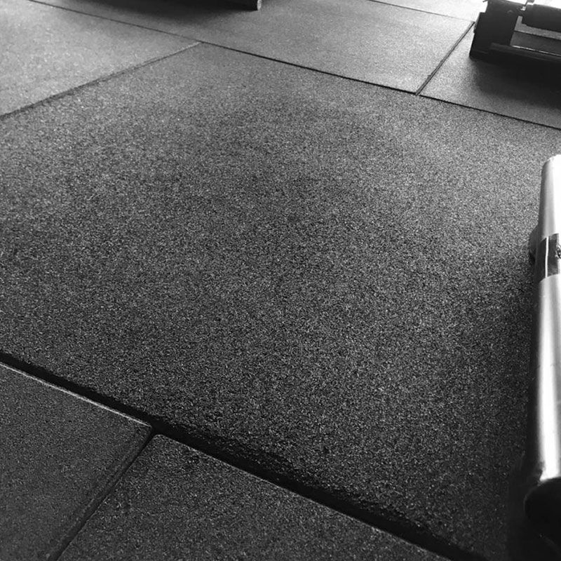 Vista de perto de pisos de borracha preta interligados, projetados para absorver impactos e proporcionar uma superfície antiderrapante.