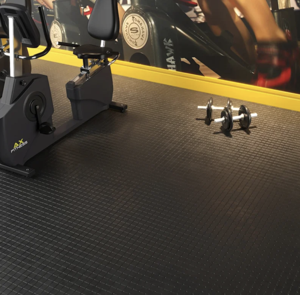 Uma academia moderna com uma bicicleta ergométrica sobre um piso de borracha preta com um padrão texturizado quadrado.