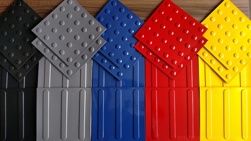 Várias placas de piso de borracha em diferentes cores, incluindo preto, cinza, azul, vermelho e amarelo. As placas apresentam texturas variadas, com algumas possuindo bolhas para maior aderência e outras com sulcos, destacando-se como opções versáteis para instalação em áreas de lazer e recreação.