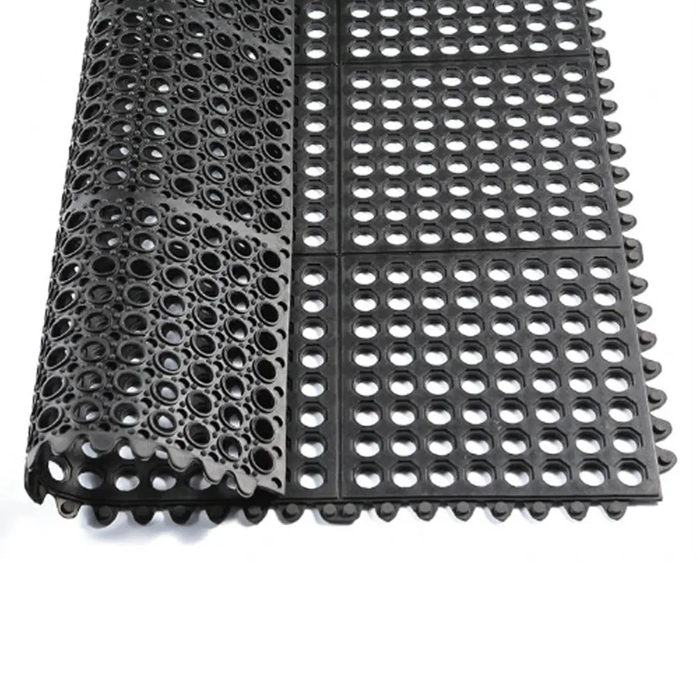 Imagem de um rolo de piso emborrachado com design perfurado, mostrando uma superfície feita de borracha preta. O material é projetado para oferecer boa drenagem e ventilação, sendo ideal para ambientes úmidos como vestiários ou áreas de treinamento ao ar livre.
