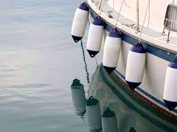 Foto de um barco ancorado na água, com várias boias penduradas na lateral, protegendo a embarcação de colisões ou para delimitar a área de circulação.
