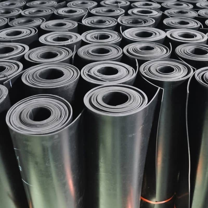 Imagem de várias rolos de lona ou fita de borracha de cor preta, organizados lado a lado em uma superfície plana, aparentando estar prontos para uso ou armazenamento industrial.