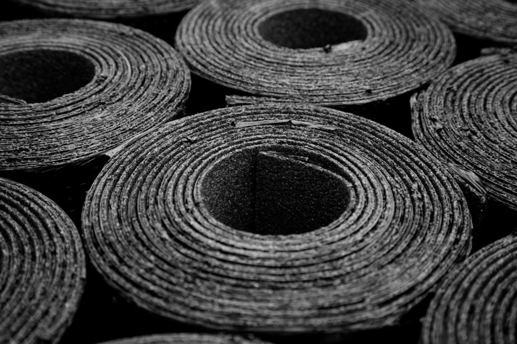 Imagem de várias tiras ou rolos de fita de borracha preta, organizadas lado a lado em uma superfície escura, apresentando uma textura firme e resistente.
