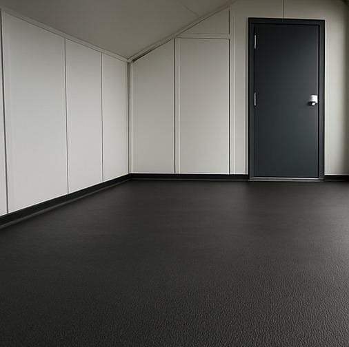 A imagem mostra um ambiente interno com piso de cor escura e paredes brancas, formando um espaço limpo e minimalista. A porta de cor escura está fechada, localizada ao lado direito da imagem. O ambiente tem um teto inclinado, sugerindo que seja um espaço sob um telhado ou no sótão de um edifício. A atmosfera é silenciosa e ordenada, possivelmente um corredor, um espaço de armazenamento ou uma área de passagem dentro de um edifício moderno.