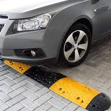 Um carro prateado passando por uma lombada modular com seções amarelas e pretas alternadas, instalada em uma superfície pavimentada de estacionamento.