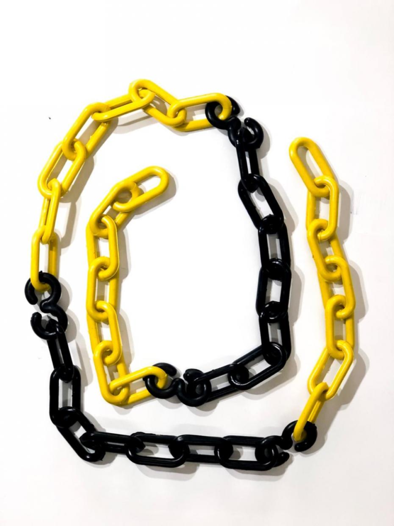 Correntes de plástico pintadas em amarelo e preto, entrelaçadas para formar a silhueta de uma letra 'C' artísticamente disposta sobre fundo branco. As correntes são de elos alongados, com alternância de cores amarelo e preto, criando um contraste visual marcante e um padrão geométrico repetitivo.