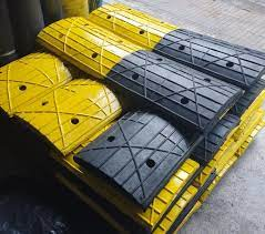 Conjunto de paletes empilhados ao lado de uma área de piso industrial. As tampas variam entre amarelo brilhante e cinza escuro, com ranhuras e furos de ventilação visíveis. A composição sugere um ambiente de depósito ou área de logística, com pallets organizados prontos para transporte ou armazenamento.