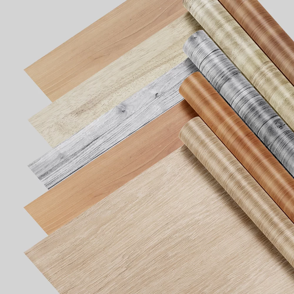 Conjunto de peças de piso em laminado com diversas texturas e acabamentos: tonalidades que variam do madeira clara ao marrom, mostra rolos de papelão destacando padrões de madeira.