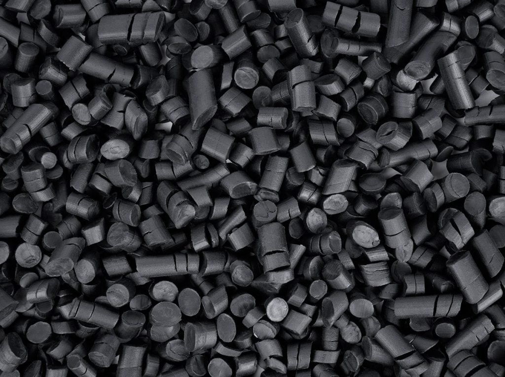 Pedaços pequenos de plastico preto em formato de cilindro. A superfície é compacta e uniforme, parecendo um monte de grânulos pretos usados em processos industriais.
