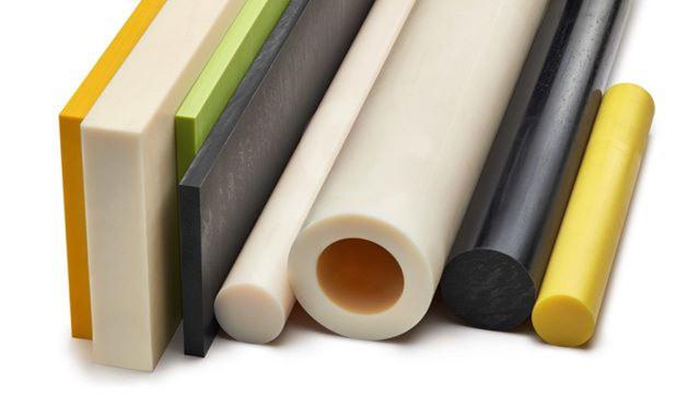 Conjunto de peças cilíndricas e planas de polímero em várias cores: blocos retangulares coloridos à esquerda, seguidos por barras lisas de diferentes diâmetros e materiais, incluindo tubos oco e cilindros sólidos. Peças em tons branco, bege, cinza, preto e amarelo, dispostas horizontalmente sobre uma superfície clara, sugerindo itens de plástico técnico usados em manufatura ou prototipagem.