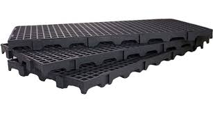 Três unidades de estrados plásticos modulares na cor preta, empilhados de forma escalonada sobre um fundo branco. A imagem destaca o design vazado da superfície em formato de grade e a estrutura inferior reforçada com pés de apoio que permitem a circulação de ar e o escoamento de líquidos.