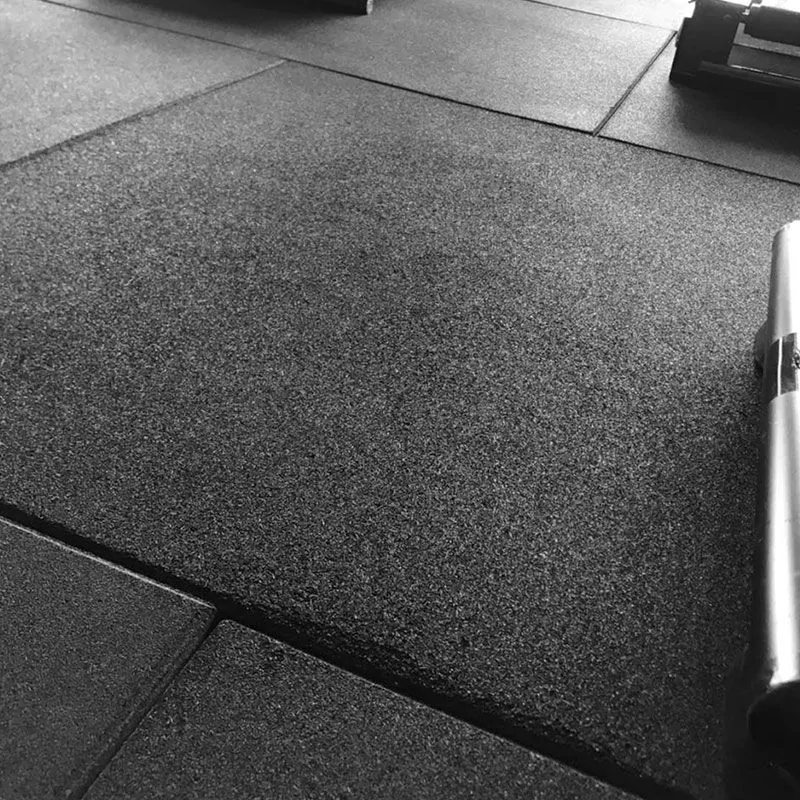 Vista de perto de pisos de borracha preta interligados, projetados para absorver impactos e proporcionar uma superfície antiderrapante.