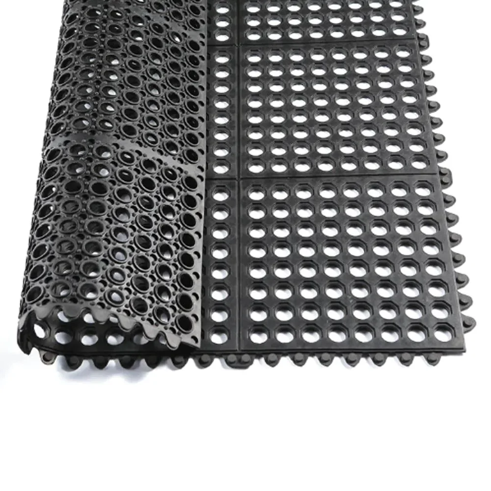 Imagem de um rolo de piso emborrachado com design perfurado, mostrando uma superfície feita de borracha preta. O material é projetado para oferecer boa drenagem e ventilação, sendo ideal para ambientes úmidos como vestiários ou áreas de treinamento ao ar livre.