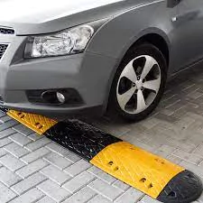 Um carro prateado passando por uma lombada modular com seções amarelas e pretas alternadas, instalada em uma superfície pavimentada de estacionamento.