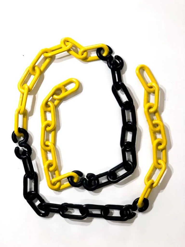 Correntes de plástico pintadas em amarelo e preto, entrelaçadas para formar a silhueta de uma letra 'C' artísticamente disposta sobre fundo branco. As correntes são de elos alongados, com alternância de cores amarelo e preto, criando um contraste visual marcante e um padrão geométrico repetitivo.