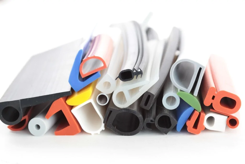 Conjunto de peças de silicone e plástico em diversas cores, cortadas em tiras e perfis de diferentes formatos, organizadas em um monte sobre uma superfície branca