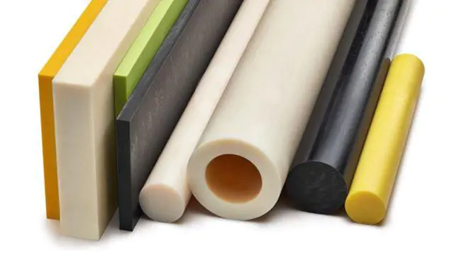 Conjunto de peças cilíndricas e planas de polímero em várias cores: blocos retangulares coloridos à esquerda, seguidos por barras lisas de diferentes diâmetros e materiais, incluindo tubos oco e cilindros sólidos. Peças em tons branco, bege, cinza, preto e amarelo, dispostas horizontalmente sobre uma superfície clara, sugerindo itens de plástico técnico usados em manufatura ou prototipagem.