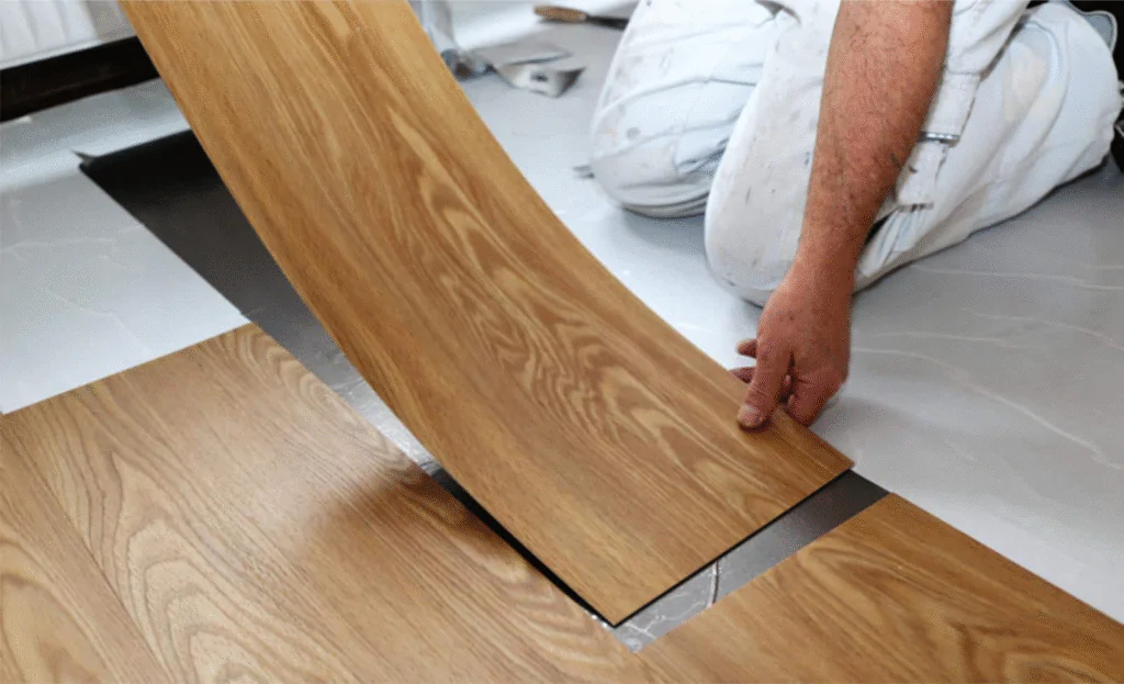 A imagem ilustra o processo de instalação de um piso vinílico amadeirado, destacando a técnica e a praticidade desse revestimento.